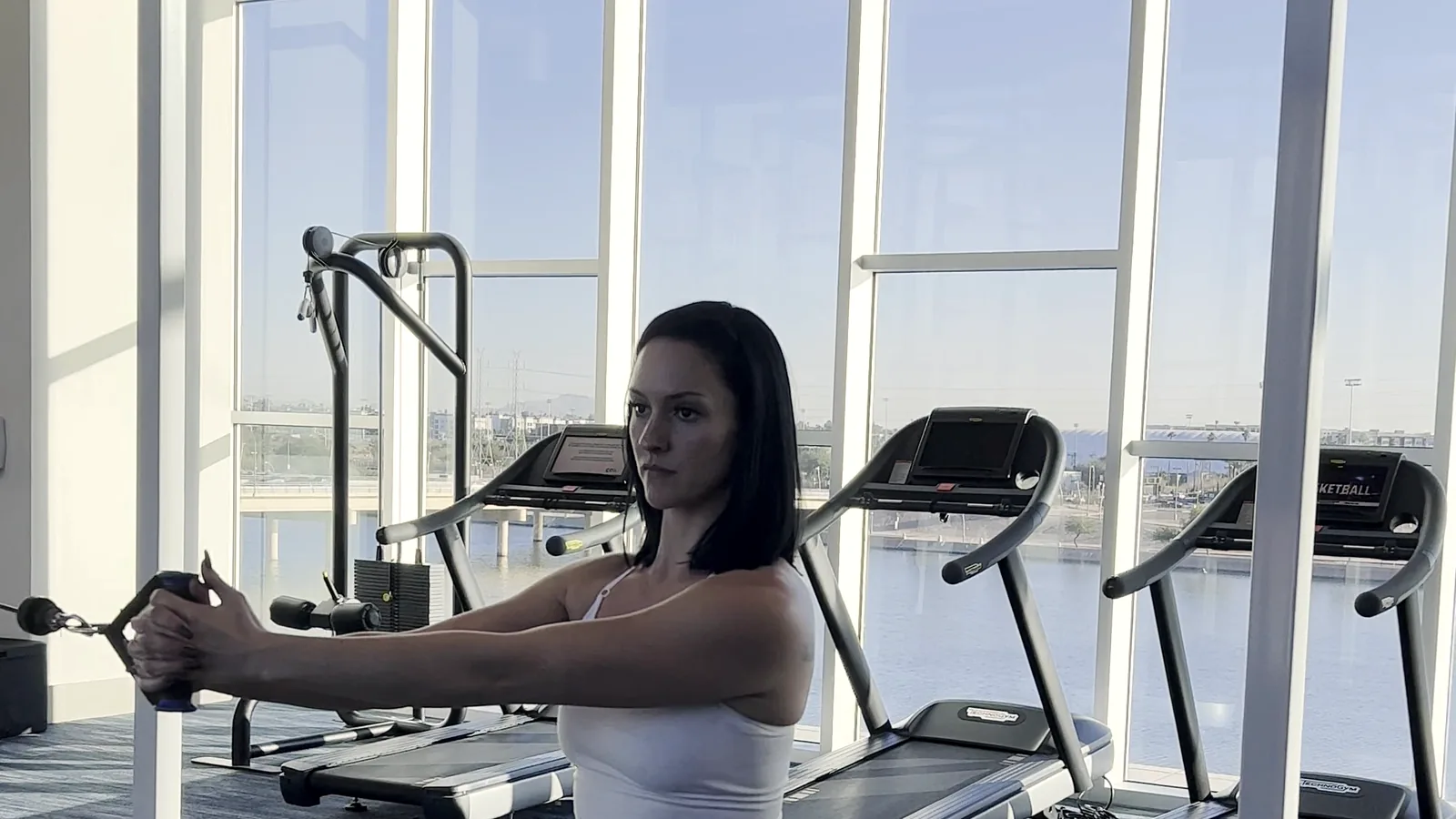 Client performing a standing cable press with braced posture in a bright private gym